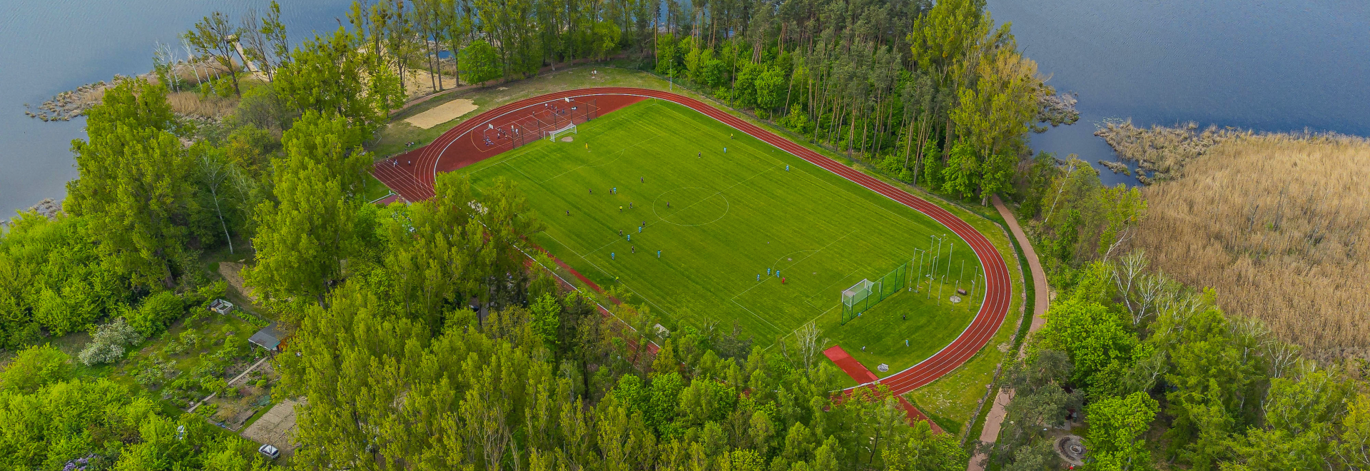 Baner wizerunkowy top Witamy w portalu GOSiR w Fabiankach, widok w g&oacute;ry na stadion otoczony drzewami